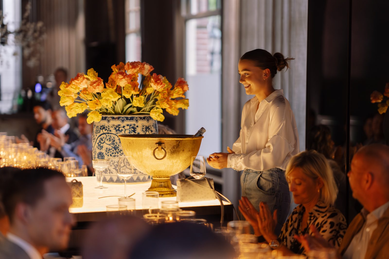 Guests seated along the candlelit table, leaning into conversation in the warm golden light